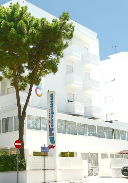 Hotel moderno bianco con balconi e parcheggio, circondato da alberi.