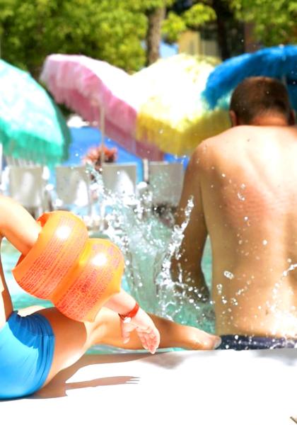 Kind und Erwachsener spielen im Pool mit orangefarbenen Schwimmflügeln.