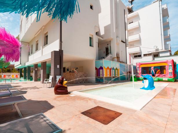 Piscina all'aperto con giochi d'acqua e lettini colorati.