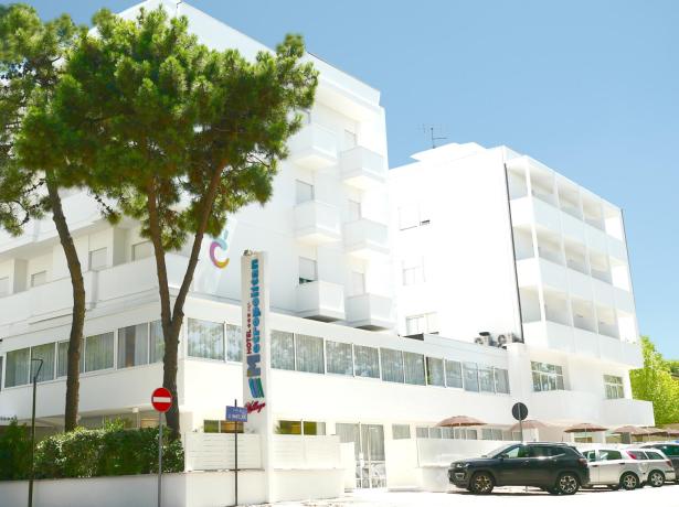 Hotel moderno e luminoso, circondato da alberi verdi e cielo blu.