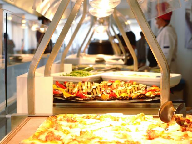 Buffet con pizza e verdure grigliate, chef sullo sfondo.