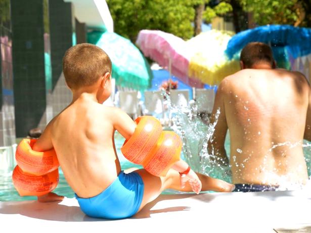 Bambino e adulto giocano in piscina con braccioli arancioni.