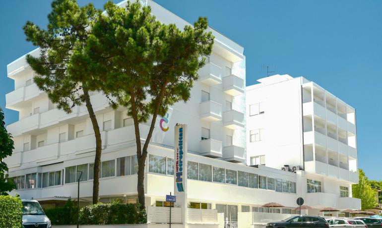 Hotel moderno a tre stelle con balconi, circondato da alberi e auto parcheggiate.