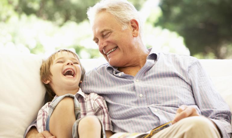 Nonno e nipote ridono insieme su un divano.