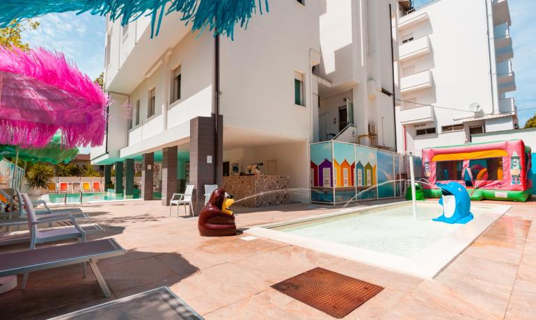 Piscina all'aperto con giochi d'acqua e lettini colorati.
