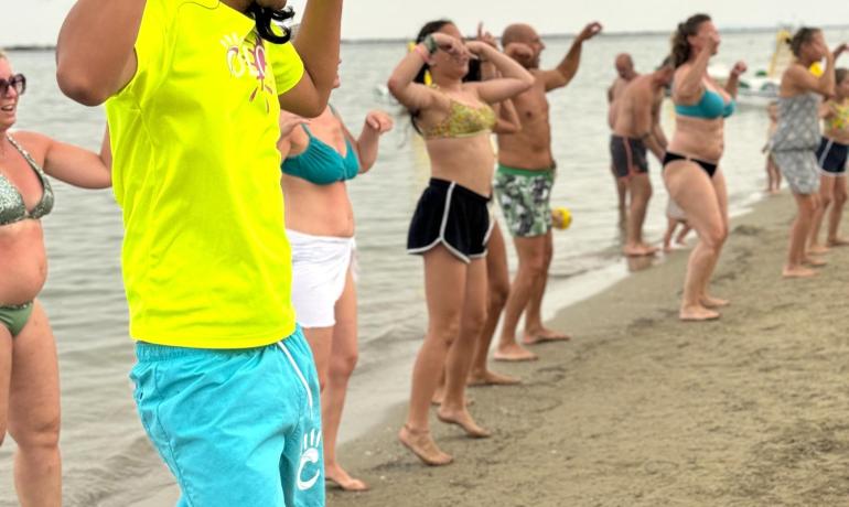 Persone fanno esercizi sulla spiaggia, guidate da un istruttore.
