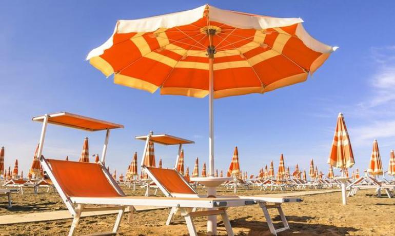 Spiaggia con lettini e ombrelloni arancioni sotto un cielo azzurro.