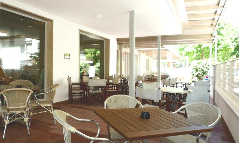 Caffetteria all'aperto con tavoli in legno e sedie bianche.