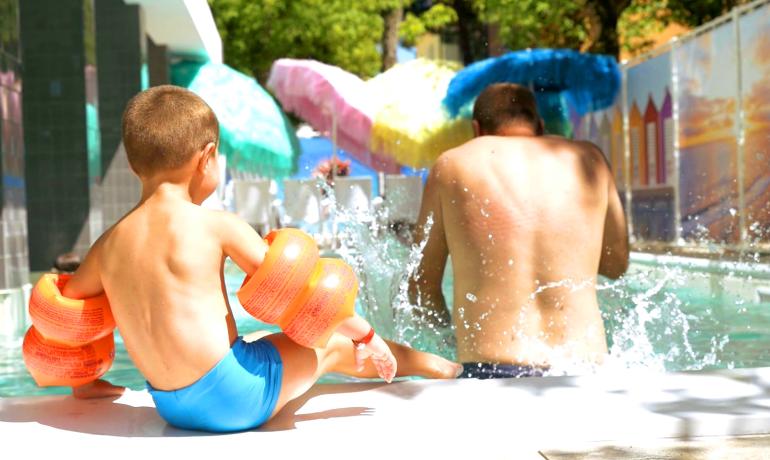 Child and adult playing in the pool with orange arm floaties.