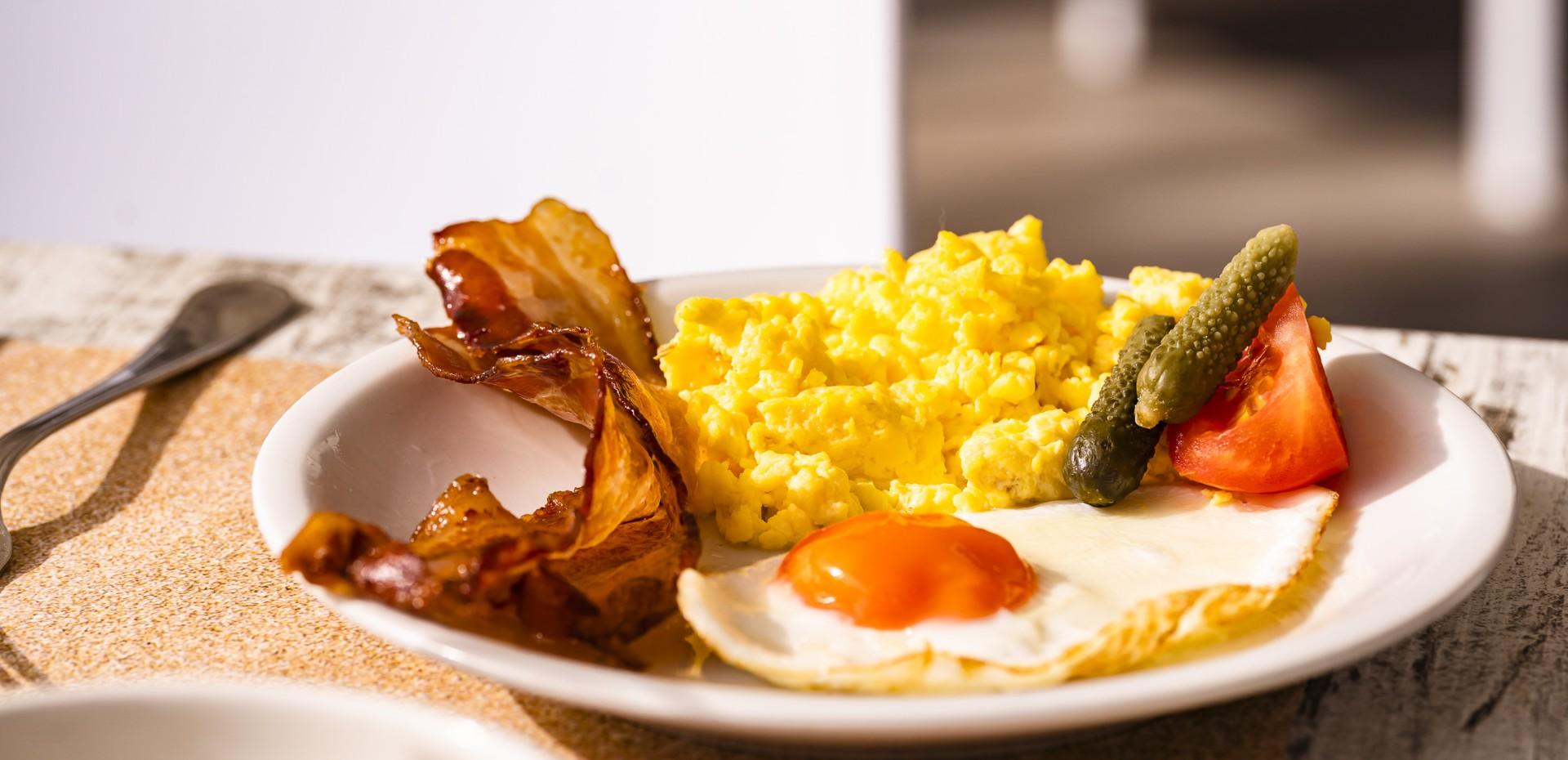 Breakfast with eggs, bacon, tomato, and pickles.