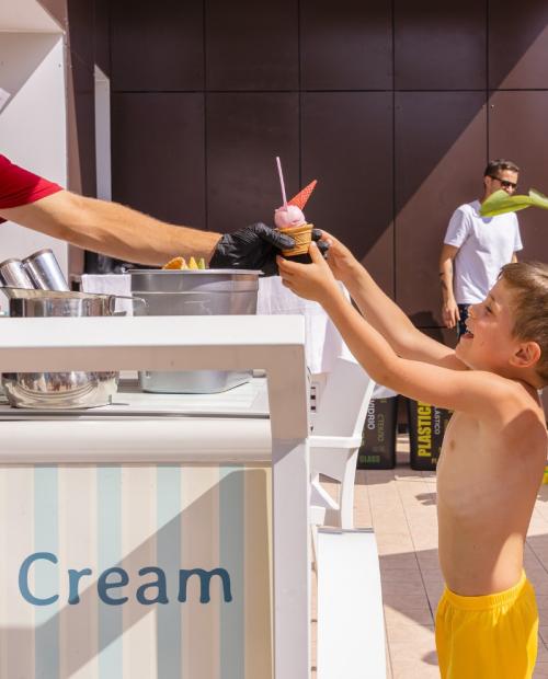 Kids receiving ice cream from an outdoor stand.