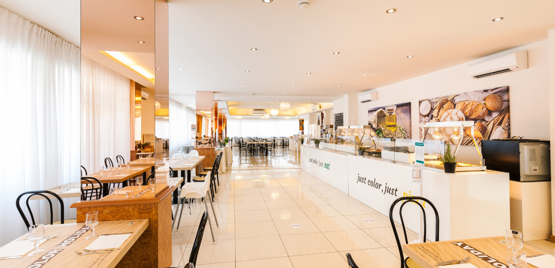 Ristorante luminoso e moderno con tavoli apparecchiati e area buffet.