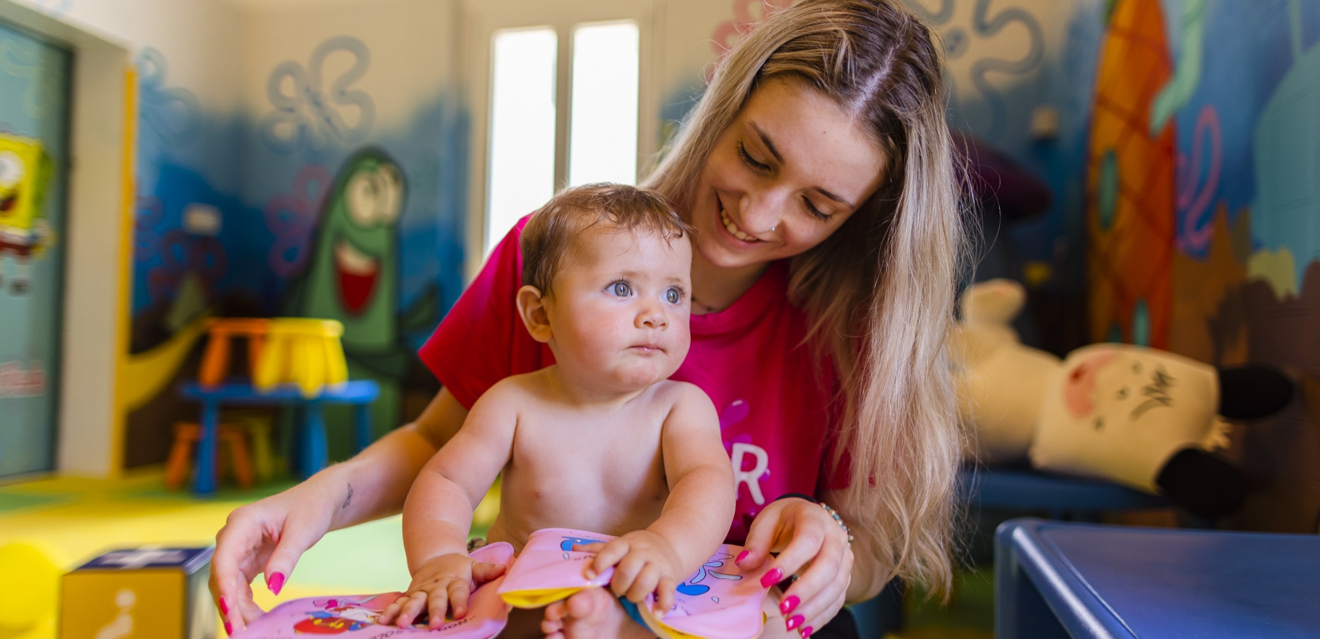 Happy baby with caregiver in a colorful, playful room.