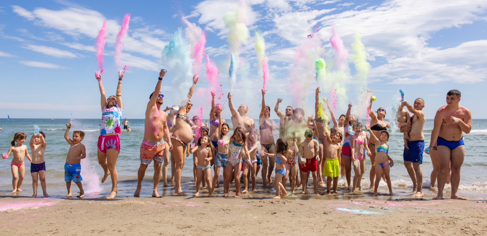 Gruppo di persone felici lancia polveri colorate sulla spiaggia, esprimendo gioia e vitalità.