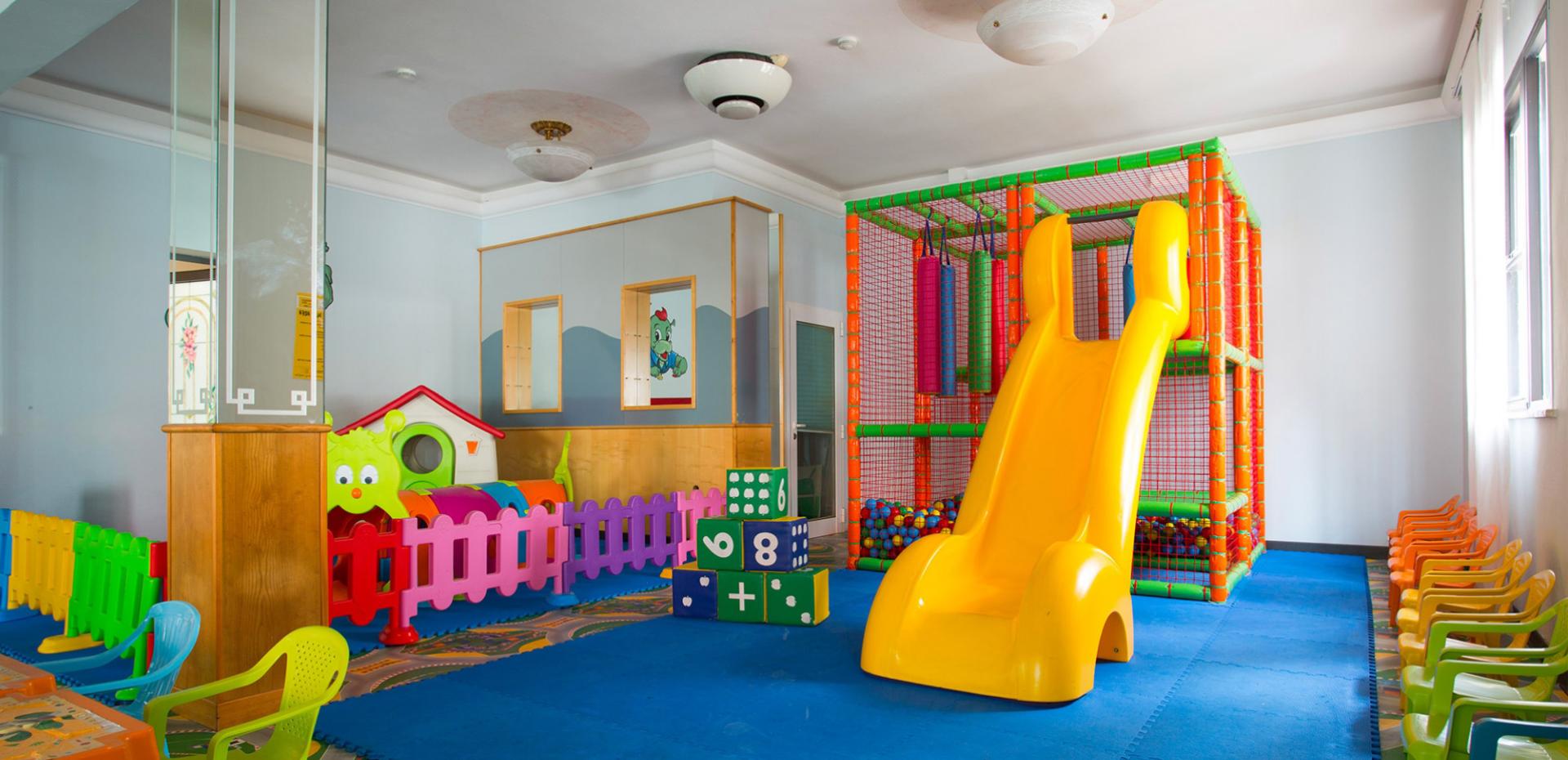 Area giochi per bambini con scivolo giallo e recinto colorato.