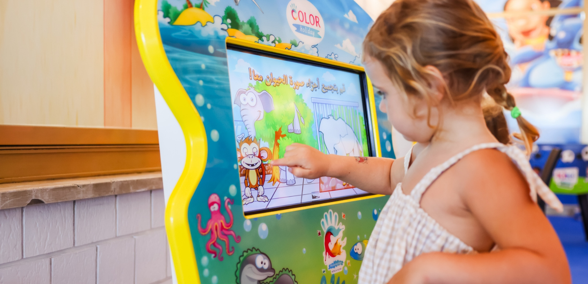 Bambina interagisce con schermo colorato, gioco educativo con animali e sfondo marino.