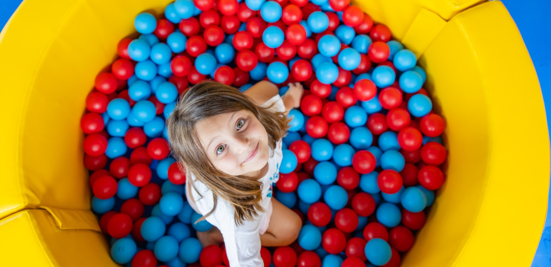 Bambina felice in una piscina di palline rosse e blu, circondata da pareti gialle.