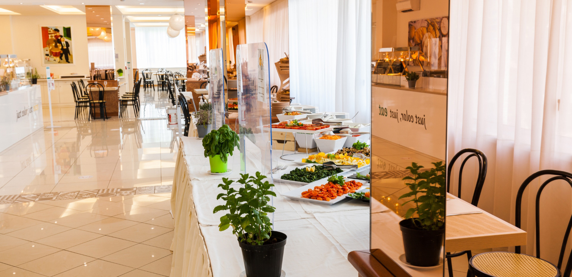 Buffet elegante con piatti colorati, sedie nere e piante decorative in un ambiente luminoso.