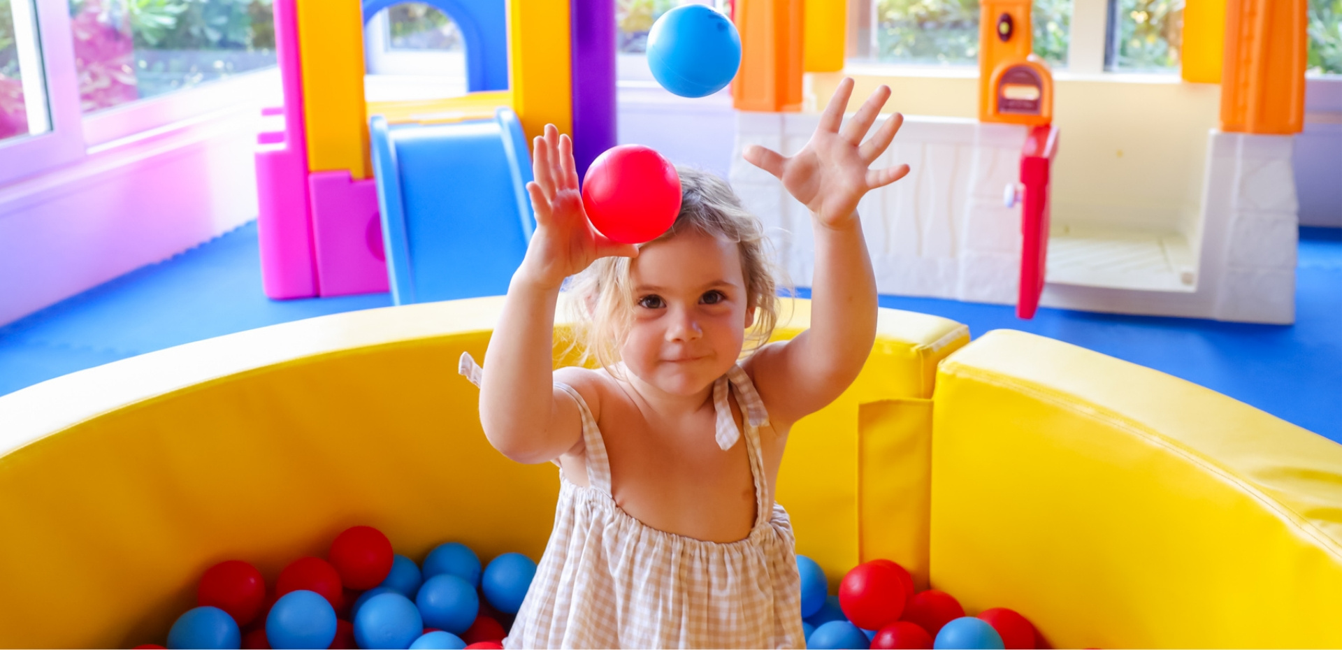 Bambina gioca con palline colorate in un'area giochi interna vivace e colorata.