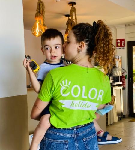 Donna con maglietta verde tiene in braccio un bambino con un giocattolo.