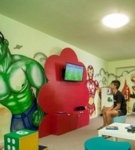 Sala giochi con supereroi, TV e arredi colorati per bambini.