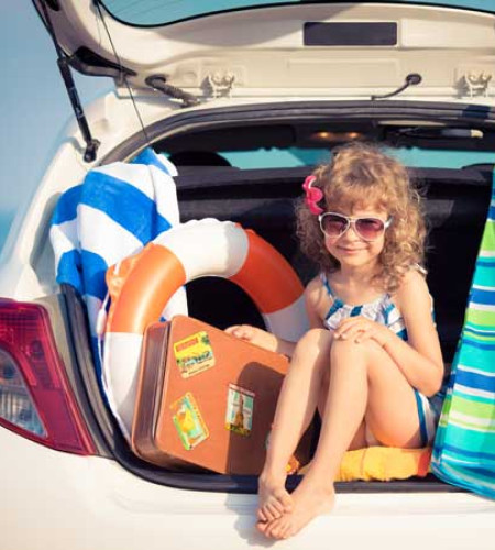 Bambina felice in auto con valigia, ombrellone e salvagente al mare.