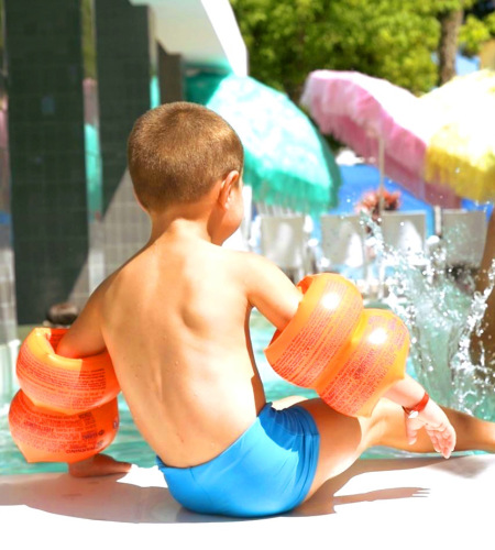 Child and adult joyfully playing in a pool under colorful umbrellas.