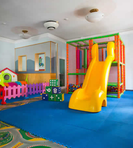 Area giochi per bambini con scivolo giallo e sedie colorate.