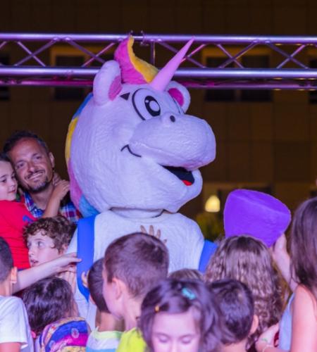 Festa con un costume da unicorno, circondato da bambini felici e sorridenti.