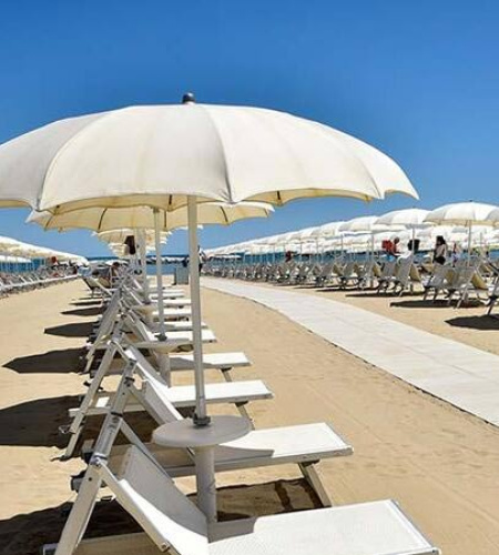 Sunny beach with white umbrellas, relaxing atmosphere, and blue sky.
