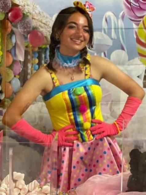 Ragazza in costume colorato da clown con sfondo di dolci e palloncini.
