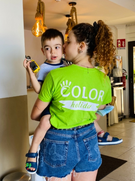 Donna con maglietta verde tiene in braccio un bambino con un giocattolo.