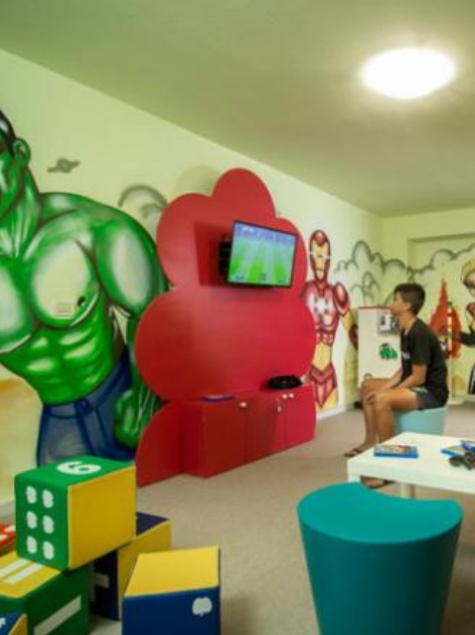 Sala giochi con supereroi, TV e arredi colorati per bambini.