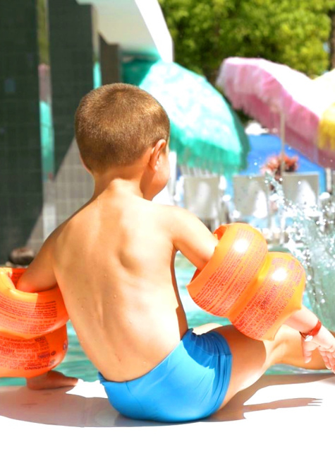 Child and adult joyfully playing in a pool under colorful umbrellas.