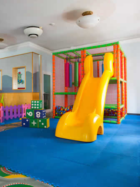 Area giochi per bambini con scivolo giallo e sedie colorate.