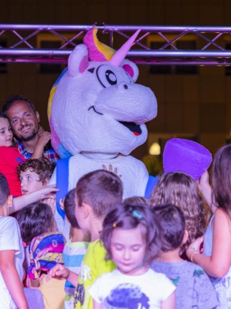 Festa con un costume da unicorno, circondato da bambini felici e sorridenti.