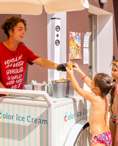 Bambini in costume prendono gelato da un venditore sorridente in una giornata soleggiata.