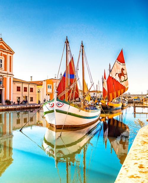 Barche storiche ormeggiate lungo un canale con edifici colorati sullo sfondo.