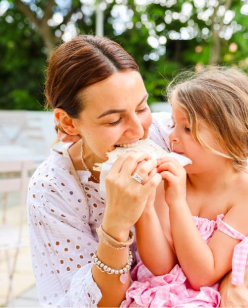 Madre e figlia condividono un momento gioioso mangiando insieme all'aperto.