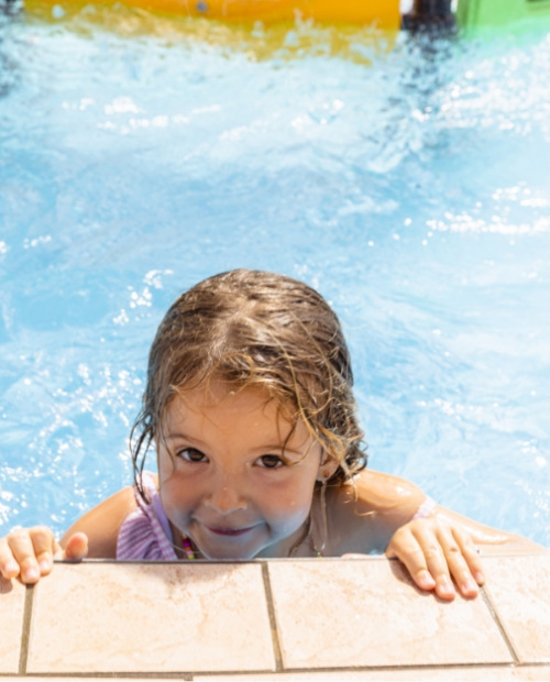Bambina sorridente si appoggia al bordo di una piscina luminosa.