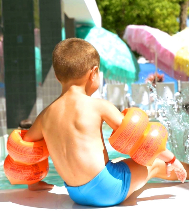 Bambino in piscina con braccioli arancioni, seduto vicino all'acqua.