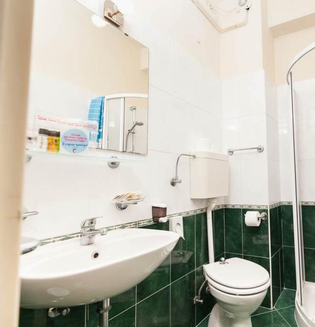 Bagno compatto con doccia angolare, lavandino, WC e piastrelle verdi e bianche.