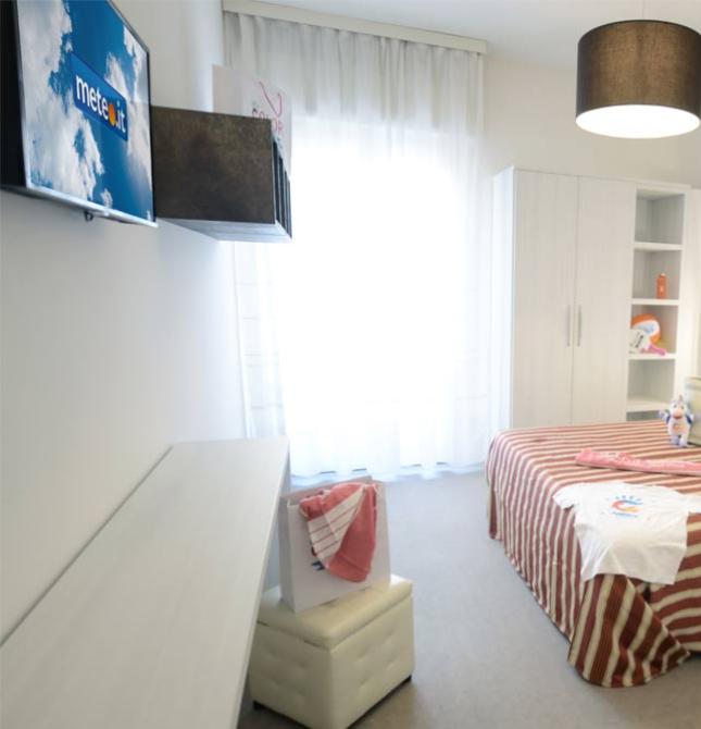 Camera moderna con letto matrimoniale, TV, valigia rossa e decorazioni bianche e rosse.