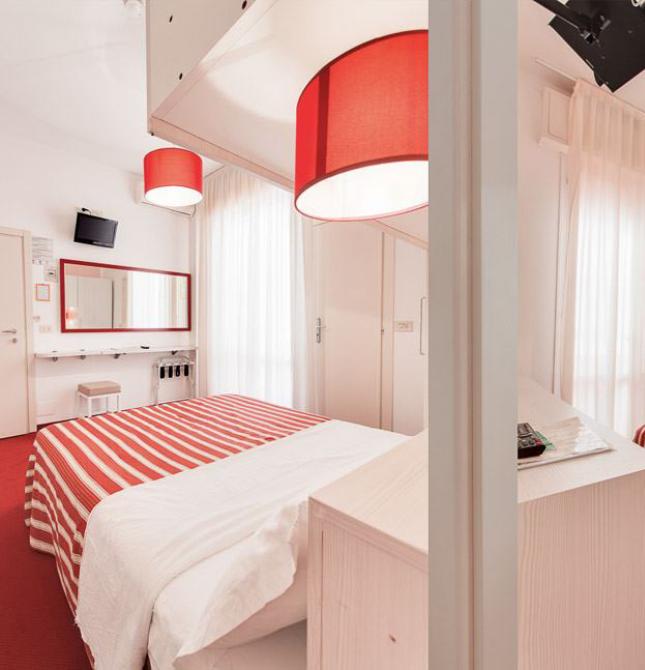 Camera moderna con letto a righe rosse, lampade abbinate e arredi bianchi.
