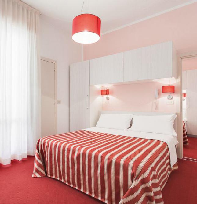 Camera da letto moderna con arredi bianchi e dettagli rossi a righe.