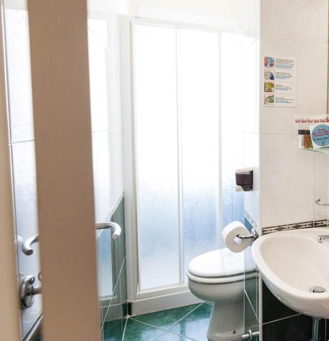 Bagno compatto con doccia, lavandino e servizi igienici, decorato con piastrelle verdi e bianche.