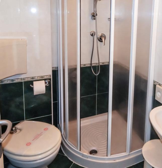 Bagno compatto con doccia, lavandino, WC e accessori da toeletta su mensola.