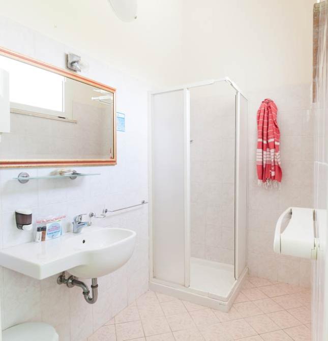 Bagno luminoso con doccia, lavandino, specchio e asciugamano rosso appeso.