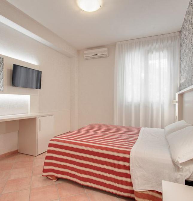 Camera moderna con letto matrimoniale, TV a parete e copriletto a righe rosse.