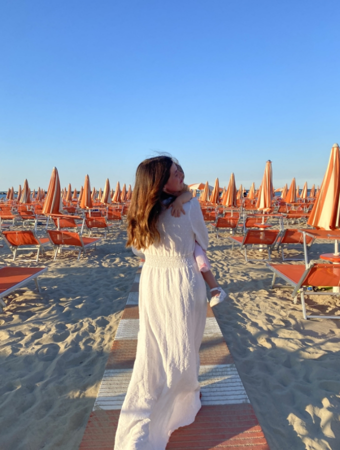 Donna con bambino passeggia tra ombrelloni arancioni su una spiaggia assolata.